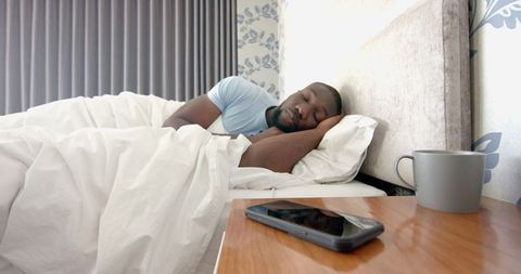 Man Sleeping Peacefully Next to Smartphone and Mug on Nightstand