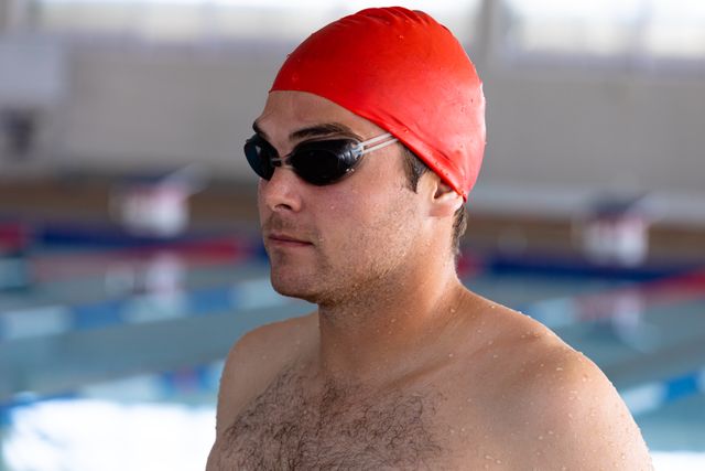 Caucasian male swimmer wearing swimming goggles and red swimming cap in a swimming pool before competing. Sports athletic competition.