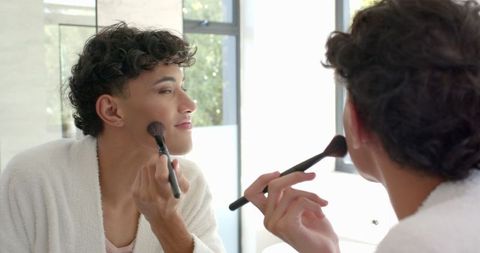Man with Curly Hair Applying Makeup at Bathroom Mirror
