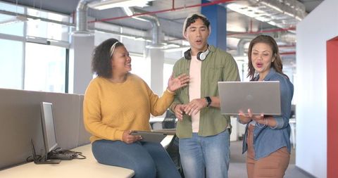 Multicultural team collaborating with laptop and tablet in modern open office workspace