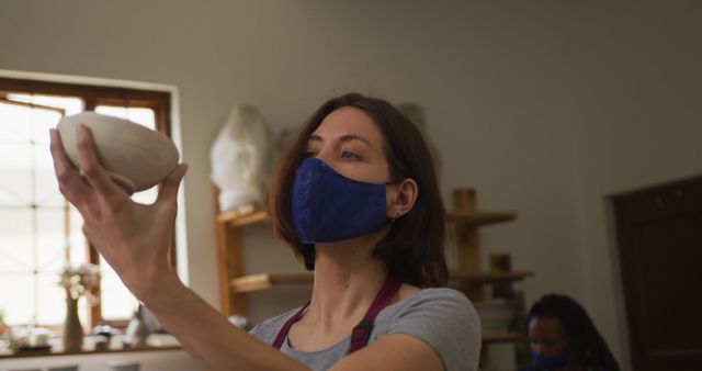 Female Potter Wearing Face Mask Examining Ceramic Bowl - Download Free Stock Images Pikwizard.com
