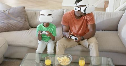 African-American Father and Son Playing Virtual Reality Games on Couch with Snacks