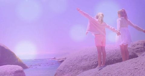 Barefoot girls exploring boulders by ocean shoreline in sunny weather
