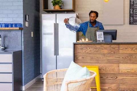 African-american barista pouring from pitcher behind wood counter in cozy modern cafe