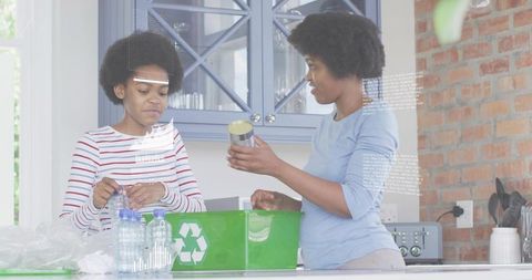 Mother and teen recycling plastic bottles and cans at kitchen counter with green bin