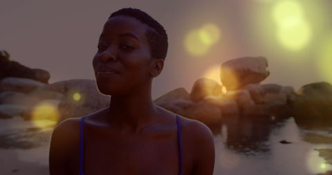 Serene Woman Strolling by Rocky Seaside with Warm Lights