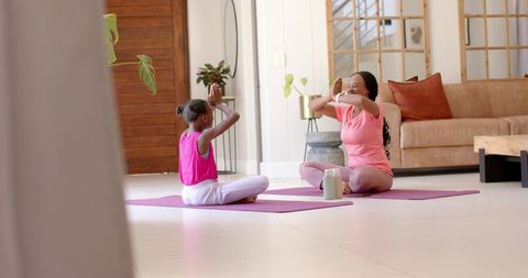 African american mother and daughter practicing yoga together at home on purple mats