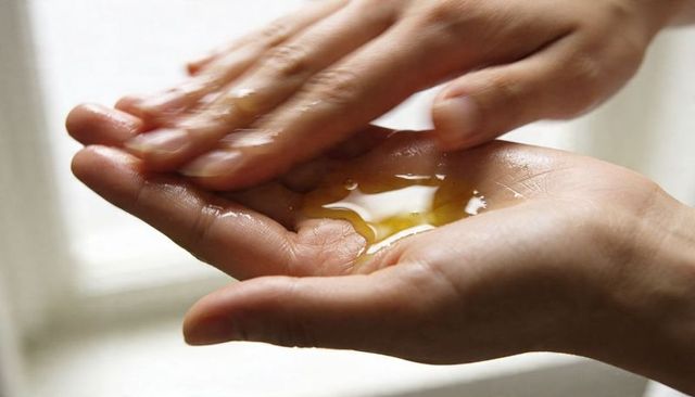 Applying nourishing hand oil in cupped palms under soft backlight for skin care routine