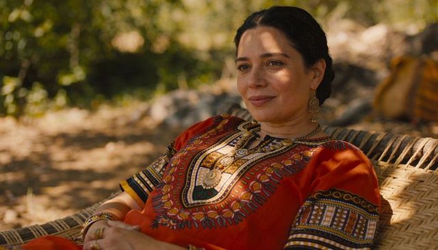 Reclining woman in embroidered orange tunic wearing gold jewelry on woven lounge chair