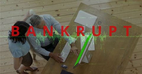 Overhead view of couple reviewing finances at home desk with bankrupt alert overlay