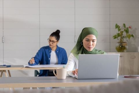 Diverse female coworkers working and studying in modern coworking space with laptop