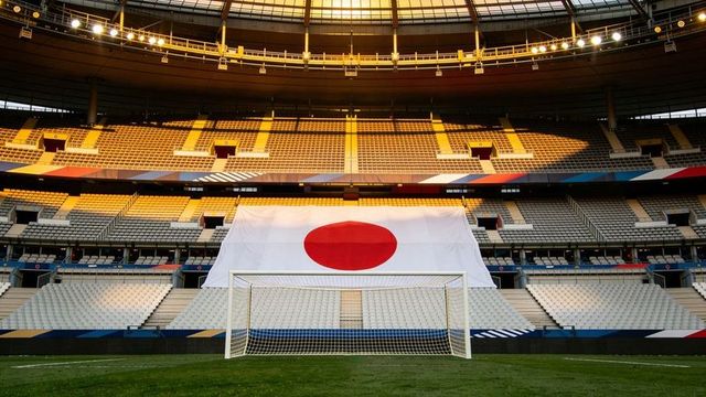 Japanese flag draping over empty stadium stands behind soccer goal on sunlit pitch