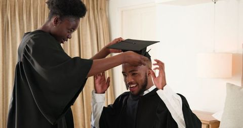 Joyful Couple Celebrating Graduation by Adjusting Cap and Gown