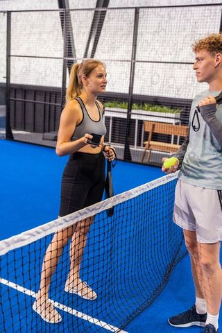 Chatting and collecting balls on blue padel court, young athletes training together