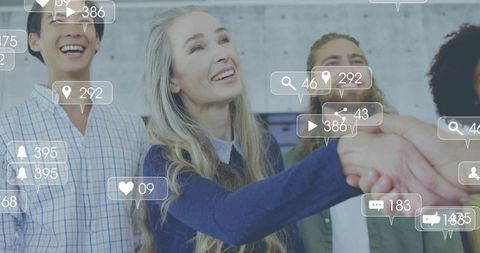 Mature professional shaking hands with team as social icons floating over workspace