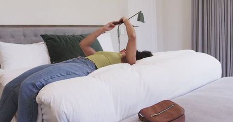 African american woman relaxing on bed using smartphone in modern bedroom