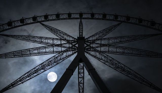 Moonlit ferris wheel silhouette looming over night sky with geometric steel spokes