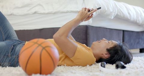 Asian Student Relaxing with Smartphone near Basketball