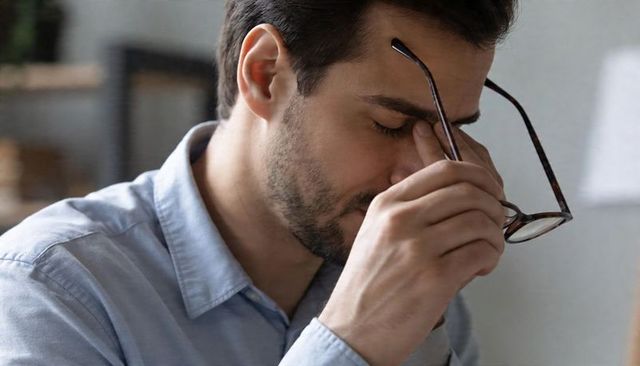 Man removing glasses and rubbing nose bridge showing workplace fatigue and stress