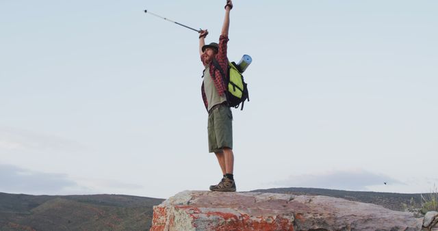 Happy caucasian male survivalist celebrating with arms in the air on mountain peak in wilderness. exploration, travel and adventure, survivalist in nature.