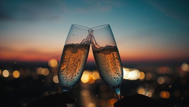 Clinking champagne flutes on rooftop at dusk with city lights