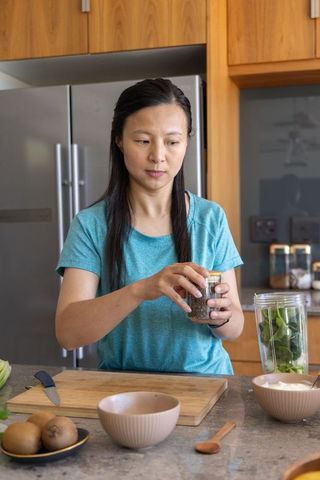 Asian woman preparing green smoothie with chia seeds and spinach in modern kitchen