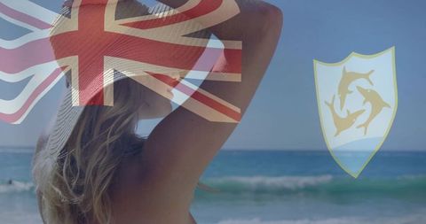 Adjusting sun hat facing ocean with union jack overlay and dolphin emblem