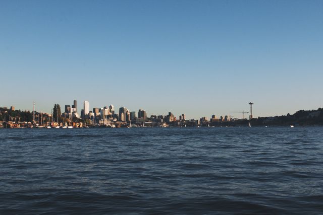 Distant view of Seattle city skyline over water under a clear sky. The iconic Space Needle stands out on the horizon. Useful for travel and tourism websites, brochures, or promotional materials related to Seattle and urban destinations. Provides a sense of calm and serenity, ideal for backgrounds in blogs or social media.