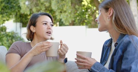 Two friends chatting over coffee on backyard sofa casual conversation relaxed patio