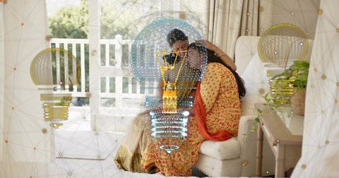 Indian mother and daughter hugging on sofa in bright home wearing sari and red dupatta