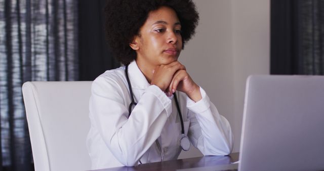 African american female doctor having a imagecall on laptop while sitting at home. distant communication and telemedicine consultation concept