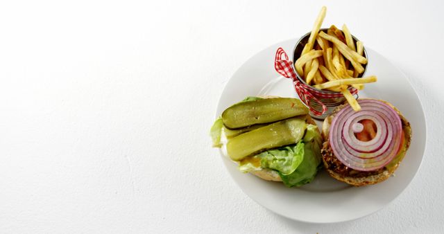 Gourmet burger with toppings including pickles and onions, served with a side of French fries on a white background. Ideal for use in advertising for fast food restaurants, menus, food blogs, or social media promotions. Highlights fresh ingredients and casual dining.