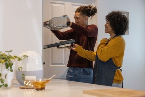 Couple baking together removing tray from oven, partner helping in cozy home kitchen