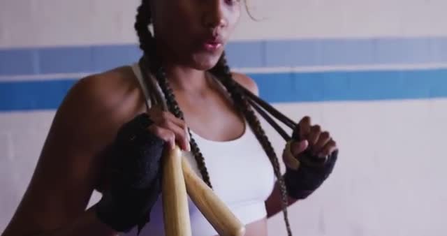 Young female boxer with braided hair holding skipping rope over shoulders in gym. Wearing athletic workout gear, she appears focused and ready for training session. Ideal for fitness, empowerment, and sport-related content highlighting perseverance and strength.