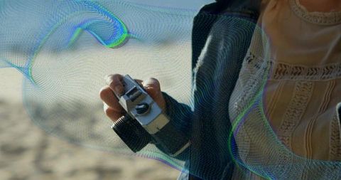 Woman holding vintage camera on a sunny beach, denim jacket