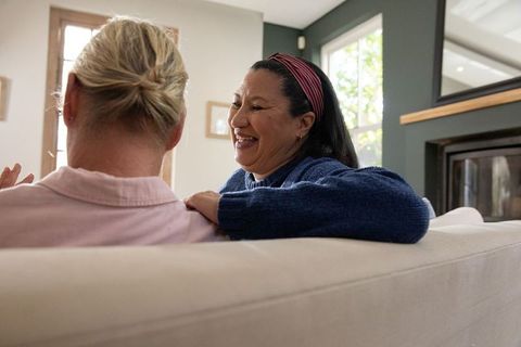 Senior friends laughing on sofa sharing warm conversation by fireplace in cozy living room