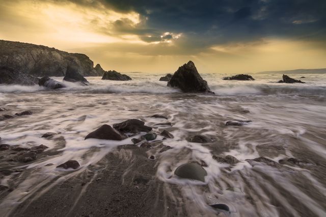 Sunset creating a dramatic effect over a rocky beach with foamy waves crashing against the shore. Perfect for coastal serenity-themed projects, nature photography collections, travel promotions, and ocean preservation campaigns.