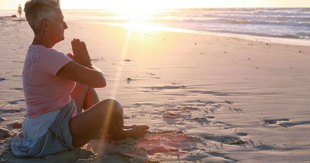 A middle-aged Caucasian woman practices yoga on the beach at sunset, with copy space. Her peaceful pose and the serene environment suggest a moment of relaxation and meditation.