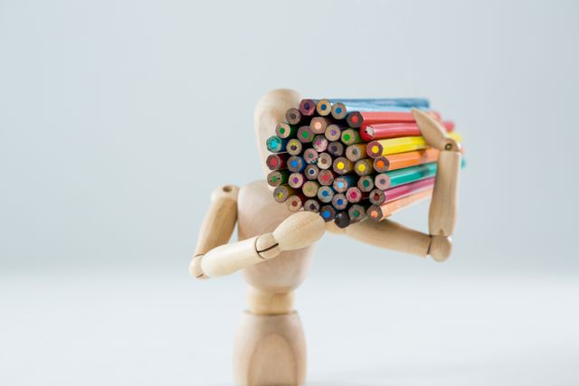 Wooden figurine carrying bunch of pencils against white background