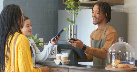 African american barista accepting mobile payment from two customers at coffee counter