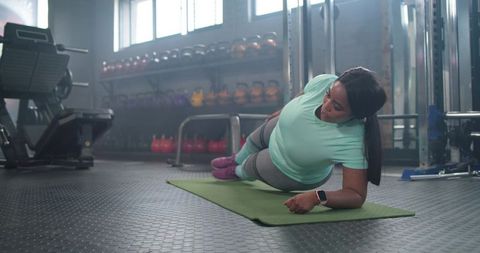 African american woman holding side plank on mat in gym building core strength and balance