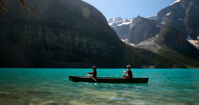 This image shows a couple canoeing on a clear blue mountain lake with towering mountains in the background. Perfect for promoting outdoor activities, adventure tourism, nature retreats, and recreational products. Can be used in travel agencies, nature conservation campaigns, and lifestyle blogs.