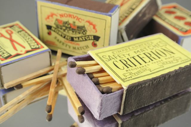 Close-up of several open vintage matchboxes spilling out safety matches onto a reflective surface. Excellent for themes related to nostalgia, collections, old-fashioned household items, or history displays.