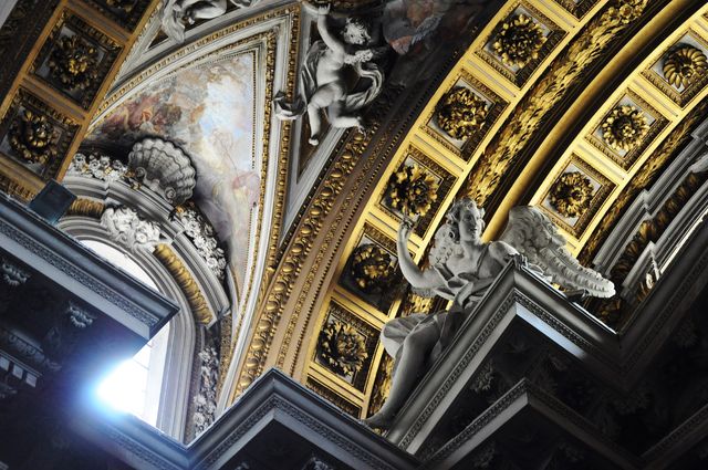 Detailed baroque church ceiling showcasing intricate carvings, statues, and golden artwork with light streaming through a window. Suitable for use in historical, religious, and cultural heritage projects, as well as in travel and tourism promotions.