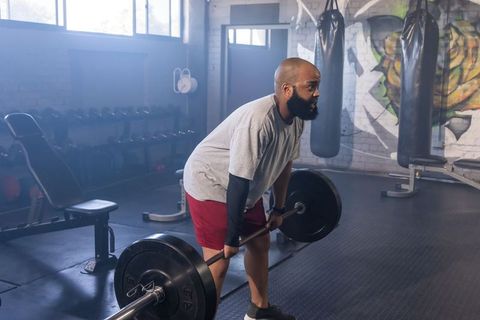 African american man lifting loaded barbell in industrial gym with graffiti mural