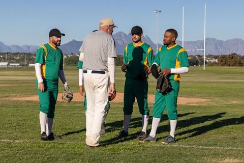 Senior coach leading baseball team huddle while players listen on sunny mountain field