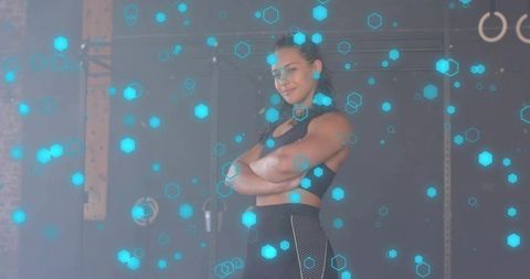 Standing confident female athlete in industrial gym with cyan hexagon digital overlay