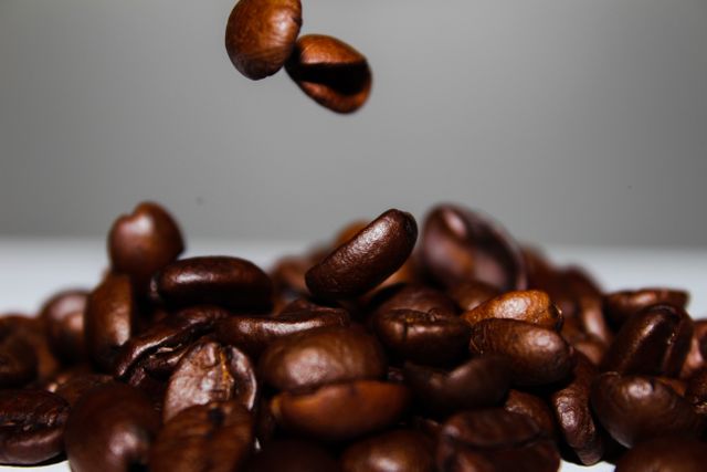 The close-up view of coffee beans dropping into a pile captures an aromatic and visually stimulating moment perfect for use in coffee-related advertisements, product packaging, food blogs, websites, and social media posts. The rich, dark shades of the beans convey freshness and high quality, making it ideal for promoting coffee shops, cafes, and gourmet products.