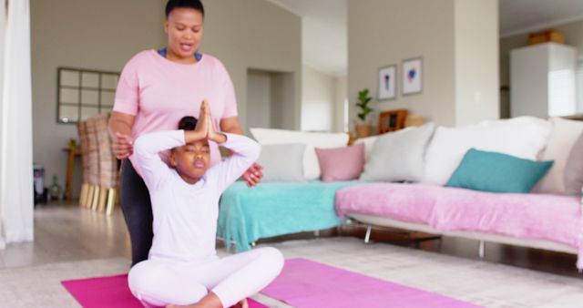 Mother is guiding child during yoga session at home on pink mat in living room. Ideal for resources about family fitness, parenting tips, healthy living guides, indoor exercises, and home activity ideas.