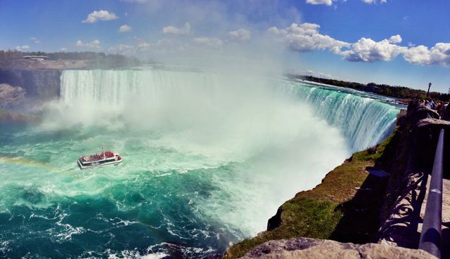 Tourist boat navigating close to raging Niagara Falls, framed by clear sunny weather and blue sky. Perfect for travel and adventure themed articles, brochures, posters, and social media content focusing on nature or famous landmarks.